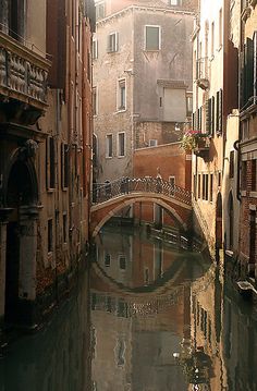 a narrow canal in an old city with buildings on both sides and a bridge crossing over it