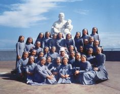 a group of women pose for a photo in front of a large white statue on top of a building