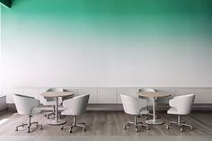 an empty room with three chairs and two tables in front of a green ombreed wall