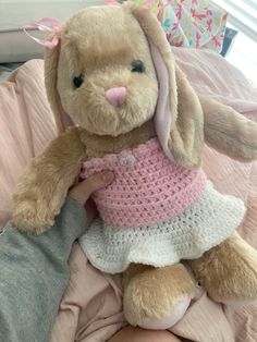 a stuffed rabbit in a pink dress sitting on a bed with someone's leg