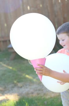 a young boy holding an ice cream cone in his hand while standing next to a giant white balloon