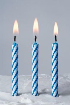 three blue and white striped candles in the snow