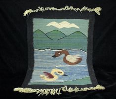 an embroidered pillow with two ducks in the water and mountains behind it on a black background