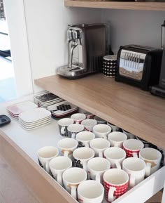 a drawer with cups in it and toaster on the top shelf next to it