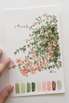 a hand holding up a piece of paper with watercolor paint and flowers on it