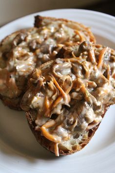 two pieces of bread with cheese and mushrooms on it sitting on a plate next to a fork