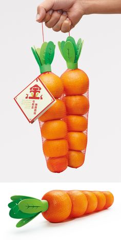 a person holding an orange shaped like a carrot with green tops and leaves attached to it