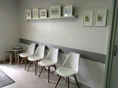 four white chairs lined up against a wall in a waiting area with pictures on the wall