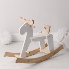 a wooden rocking horse next to balls of yarn on the floor in a white room