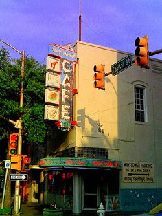 the corner of an intersection with traffic lights and a building in the background that has many signs on it