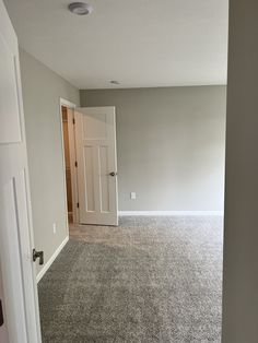 an empty room with carpeted flooring and white door in the center, looking into another room