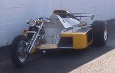 a yellow and silver motorcycle parked next to a white wall with a building in the background