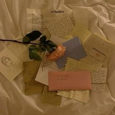 a rose is sitting on top of some papers and letters that are all over the bed