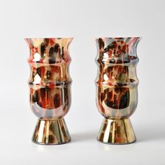 two shiny vases sitting next to each other on a white surface with no one around them