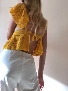 a woman wearing white pants and a yellow crochet top is posing for the camera