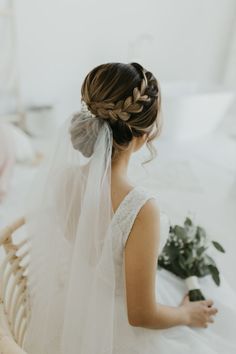 a bride sitting on her bed looking at the flowers in her hair and veil over her head