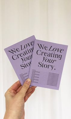 someone holding up two purple cards with the words we love creating your story on them