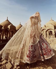 a woman in a wedding dress is standing on the side of a hill with an intricately designed veil