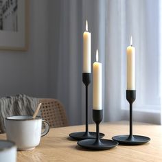 three lit candles sitting on top of a wooden table next to a cup and saucer