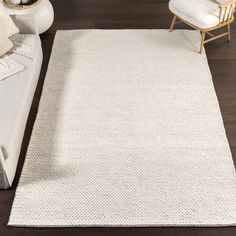 a white rug on top of a wooden floor next to a couch and chair with pillows