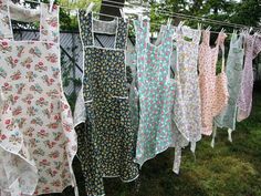 many different colored aprons hanging on a clothes line in front of some trees and bushes