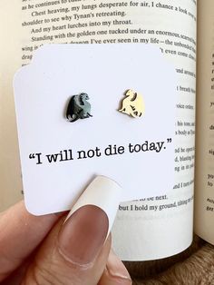 a person is holding up a book with two small animal earrings on top of it