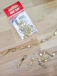 there are several pieces of gold chain on the wooden table next to it is a package of metal clips