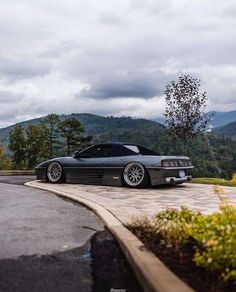 a black car parked on top of a parking lot next to a lush green hillside