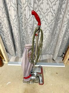 a red and silver vacuum is on the floor in front of a curtained window