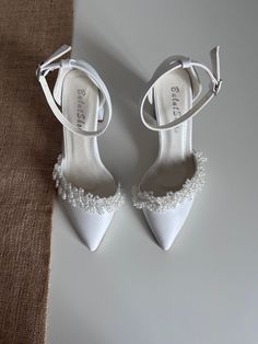 a pair of white high heeled shoes sitting on top of a table next to a piece of cloth