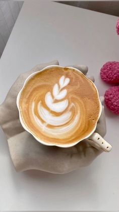 a person holding a cup of coffee on top of a white table next to raspberries