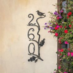 a wrought iron bird and flower decoration on the side of a building with pink flowers