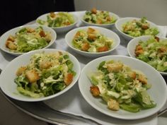 many white bowls filled with salad on top of a table next to silver trays