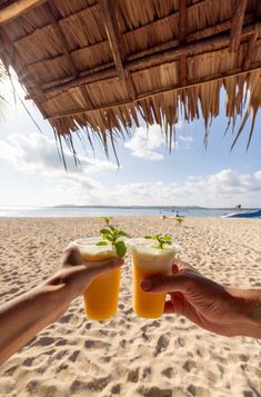 two people toasting on the beach with orange juice in front of them and straw umbrellas