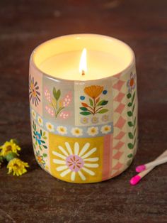 a lit candle sitting on top of a wooden table next to flowers and two spoons