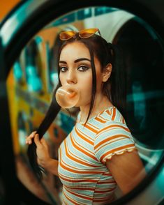 a woman with long hair and sunglasses blowing bubbles in front of a mirror