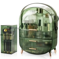 a green glass container with gold trimmings next to a clear case filled with cosmetics