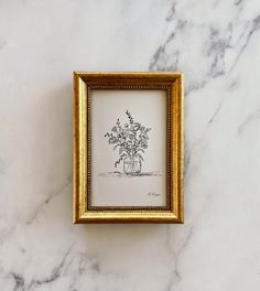 a gold frame with a drawing of flowers in it sitting on a marble countertop