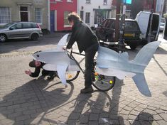 a man on a bike with a shark shaped body attached to the back of it