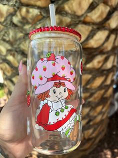 a person holding up a glass cup with strawberries on it and a straw hat