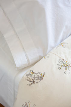 an unmade bed with white linens and yellow flowers on the comforter cover