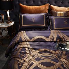 a bed with purple and gold comforters on top of it next to a night stand