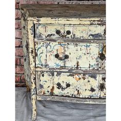 an old painted chest of drawers with peeling paint on the top and bottom, in front of a brick wall