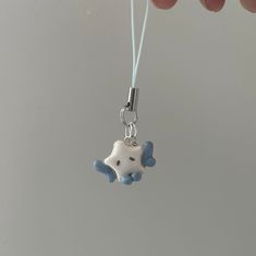 a hand holding a tiny blue and white teddy bear charm on a string with a bead