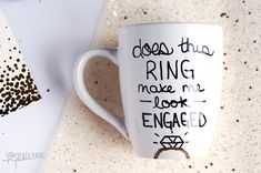 a coffee cup with writing on it sitting next to a piece of paper that says, does this ring make me look engaged?