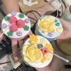 two cakes decorated with flowers and berries are being held by someone's hands in front of them