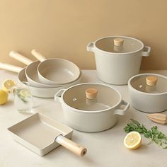 several pots and pans on a table with lemon slices, parmesan sprigs and wooden utensils