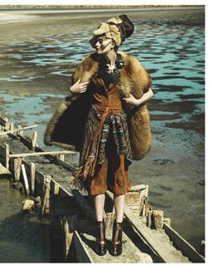 a woman is standing on a dock with a fur coat over her shoulders and boots