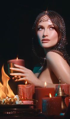 a woman holding a lit candle in front of some candles on a table with other items around her