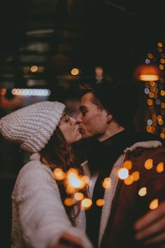 a man and woman kissing in front of christmas lights